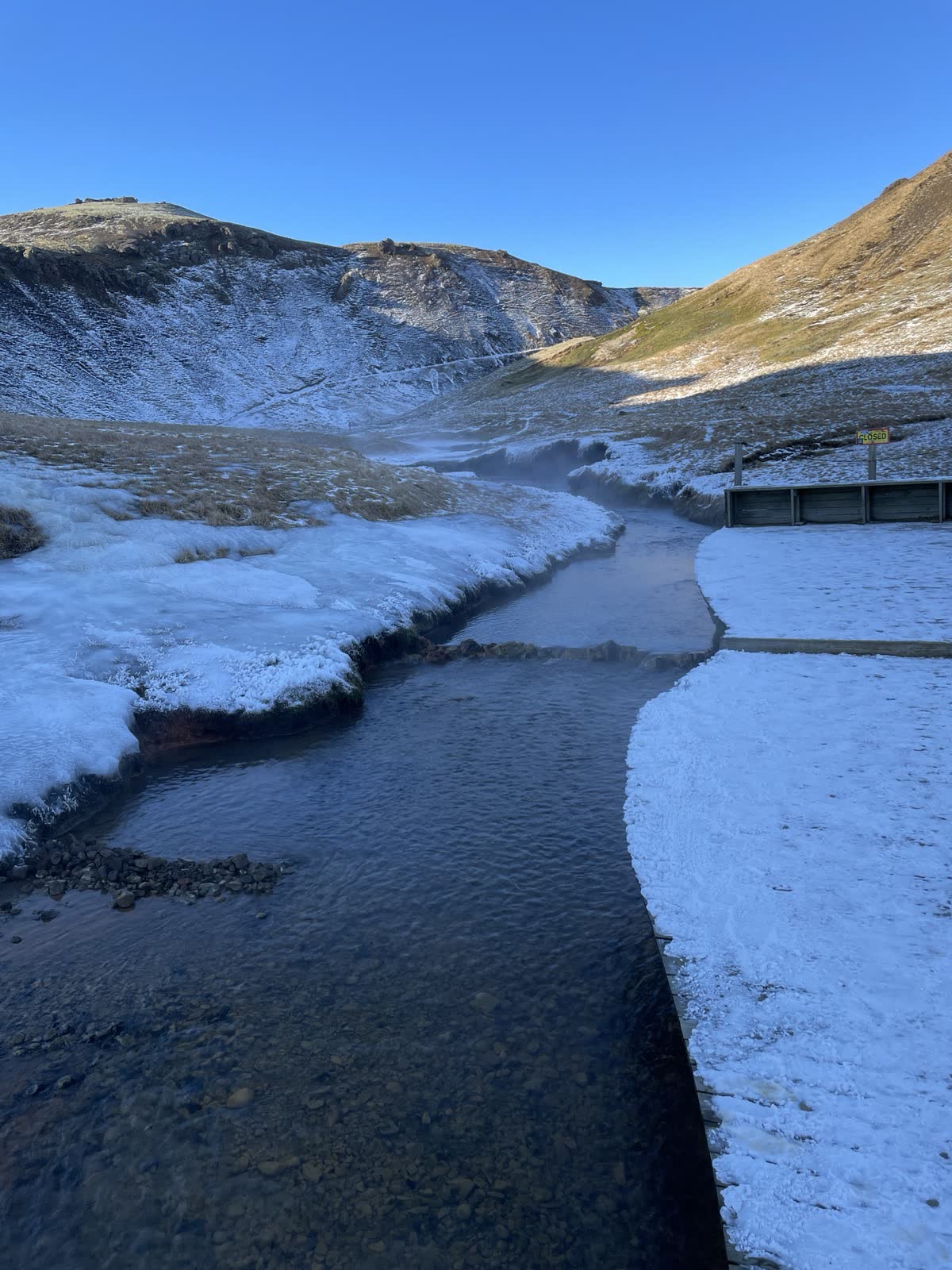 Reykjadalur 溫泉河冬季實景,河道旁有積雪與寫着 CLOSED 的告示;